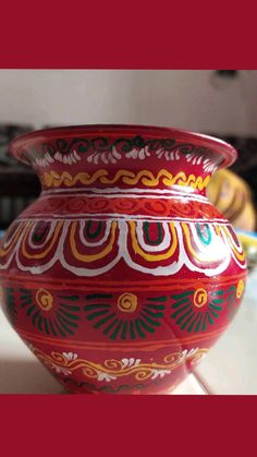 a red vase sitting on top of a counter next to other bowls and dishes in the background