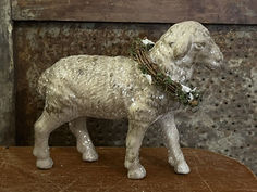 a statue of a sheep with a wreath around its neck on a wooden table in front of a rusty wall