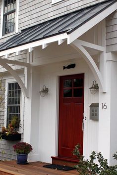 a white house with a red door and some plants on the front porch, next to it is a potted plant