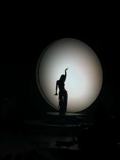 a woman standing in front of a large white ball on top of a dark stage