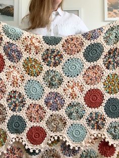 a woman is holding up a crocheted granny's afghan in front of her