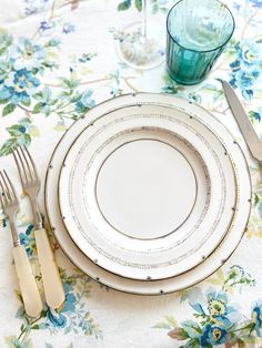 a table set with plates, silverware and glasses on top of a floral table cloth