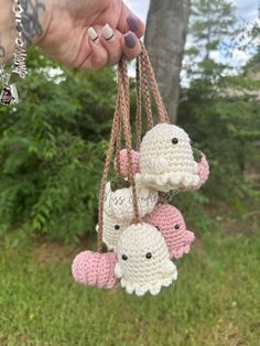 a hand holding three small crocheted elephants hanging from strings in front of trees