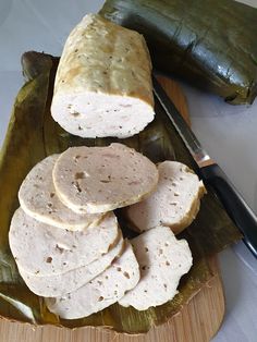 sliced meat on a banana leaf next to a knife