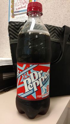 a bottle of dr pepper soda sitting on top of a white counter next to a black bag