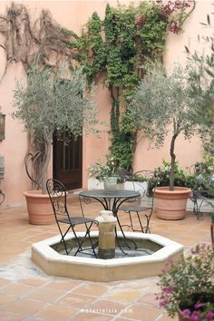 Charming Mediterranean patio with a small fountain, wrought iron chairs, and potted trees.