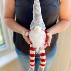 a woman holding a crocheted gnome hat with a red and white striped leg