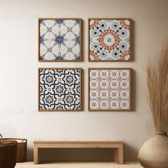 three square tiles are hanging on the wall next to a wooden bench and vase with dry grass