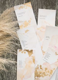 four pieces of paper with gold foil on them sitting next to some dry grass and a plant