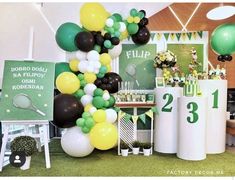 a table topped with lots of balloons next to tall white and green pillars filled with decorations