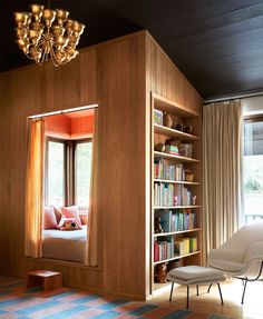 a room with a chair, bookshelf and window in the corner that is open