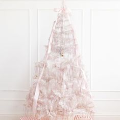 a white christmas tree with pink ribbons and bows on it's head, sitting in front of a wall