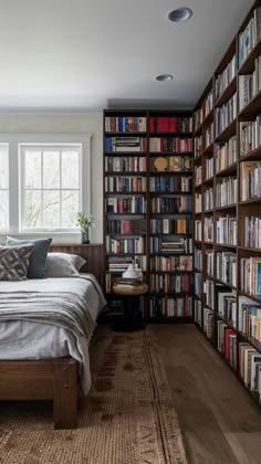 a bed sitting in front of a book shelf filled with books next to a window