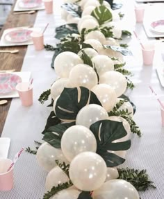 a long table with white balloons and greenery