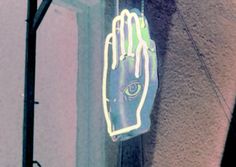 a neon sign hanging from the side of a building with an eye on it's hand