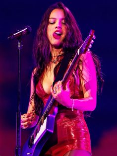 a woman holding a guitar while standing in front of a microphone