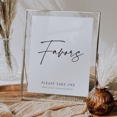 a glass frame with the word favors written in cursive writing on it next to some dried plants