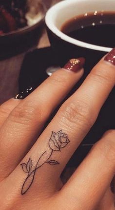 a woman's hand with a small rose tattoo on the middle finger, next to a cup of coffee