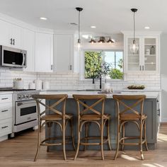 a kitchen with three stools at the center of the island and an oven in the back