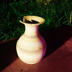 a white vase sitting on top of a wooden table next to green grass and flowers