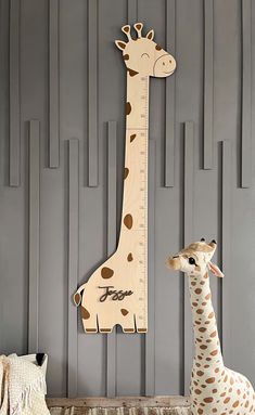 a giraffe standing next to a tall wooden growth chart on a gray wall