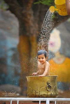 a baby sitting in a bucket with water pouring out of it