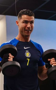 a man holding two black dumbs in his hands and smiling at the camera while wearing a blue shirt