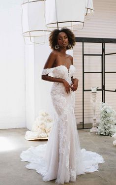 a woman in a white wedding dress standing next to a chandelier with flowers on it