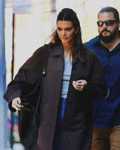 a woman walking down the street with a man in blue shirt and black coat behind her