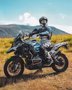 a man riding on the back of a motorcycle down a dirt road next to a lush green hillside