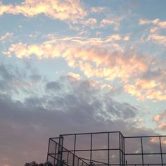 the sky is filled with clouds above a baseball field and fenced in area for batting practice