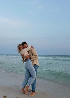 two people hugging on the beach with waves in the background