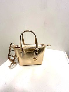 Michael Kors Jet Set Travel XS Carryall Tote Satchel Shoulder Crossbody Bag in Gold About the item Material: Vegan Leather Color: Gold Authenticity: 100% Authentic Features: Michael Kors Logo at the front 1 MK Charm Silver-Toned Hardware Zip Top Closure Slip-in Pocket One MK Charm Custom Fabric Lining 1 Slip-in Pocket, 1 Zipper Pocket Dimensions: 9" (top) 11" (bottom) x 7.75" (H) x 4.25" (D) Strap Length: 5" (hand carry), 24" (shoulder carry)Description Style: Stylish and functional for busy women. Material: Made from vegan leather with a coated finish. Storage: Offers plenty of space with inner pockets, a slip-in pocket, and a zipper pocket. Extras: Comes with a detachable strap, brand card, and bag charm. Size: Compact size measuring 7.75 inches in height and 4.25 inches in depth. Accent Michael Kors Gold Bag With Adjustable Strap, Gold Michael Kors Bag With Adjustable Strap, Michael Kors Gold Shoulder Bag With Removable Pouch, Michael Kors Gold Double Handle Shoulder Bag, Gold Michael Kors Shoulder Bag With Double Handle, Michael Kors Gold Double Handle Bag, Michael Kors Gold Tote Bag, Michael Kors Gold Shoulder Bag With Handles, Michael Kors Gold Bag With Handles