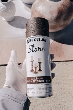 a person holding up a can of rustoleum to some kind of stone sculpture