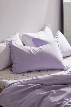 a bed with purple sheets and pillows on top of it in front of a window