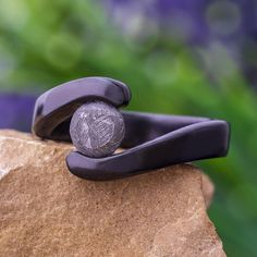 a pair of black metal scissors resting on top of a rock with purple flowers in the background