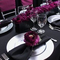 the table is set with black and white plates, silverware, and purple flowers