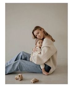 a woman sitting on the ground holding a baby in her lap and some wooden toys