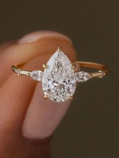 a woman's hand holding an engagement ring with two pear shaped diamonds