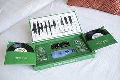 an open green box containing two vinyl records and a pair of sunglasses, sitting on a bed