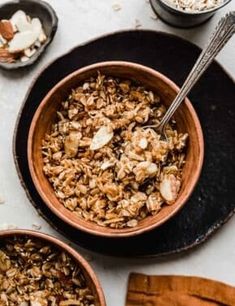 two bowls filled with granola on top of a table next to wooden spoons