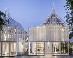 an architecturally designed house with white walls and glass windows at night, surrounded by greenery