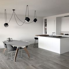 a modern kitchen and dining room with white walls, wood flooring and black pendant lights hanging from the ceiling