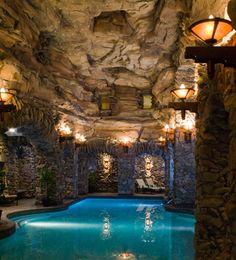 an indoor swimming pool surrounded by stone walls and lights on the ceiling, with a waterfall in the middle