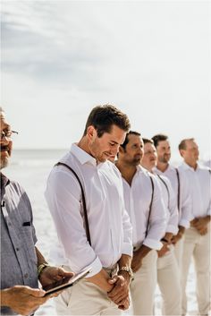 a group of men standing next to each other in white shirts and ties on the beach