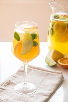 a pitcher and glass filled with liquid next to sliced oranges on a white table