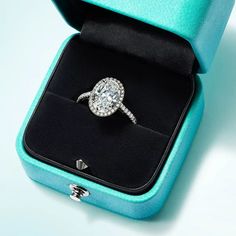 an engagement ring in a blue box with its lid open and the diamond set on it's side