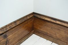 the corner of a room with wood flooring and white painted walls, along with wooden planks