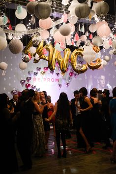 a group of people standing in front of a wall with balloons hanging from it's ceiling