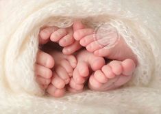 two newborn babies are laying in a blanket together with their hands on top of the baby's feet